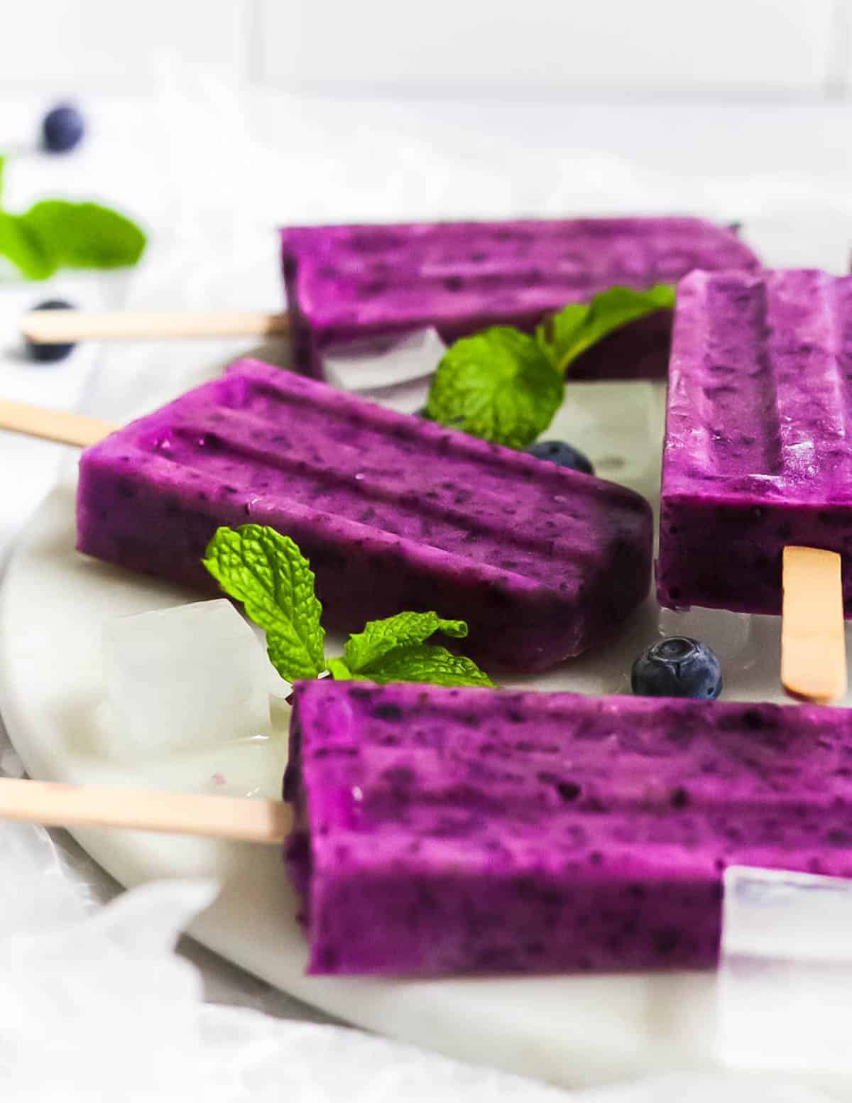 Side view of four berry ice pops. Garnished with fresh mint and blueberries