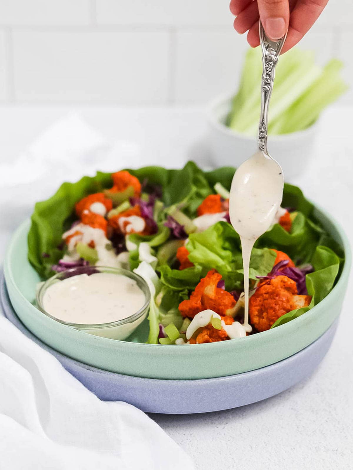 Picture of 3 buffalo cauliflower lettuce wraps with a spoon drizzling ranch on top of one of the wraps.