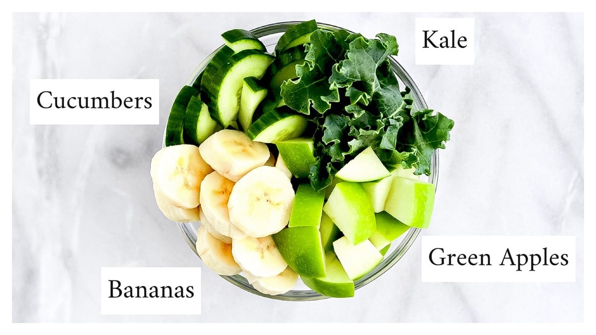 Picture of a glass bowl filled with kale, cucumbers, banana slices, and a chopped green apple.