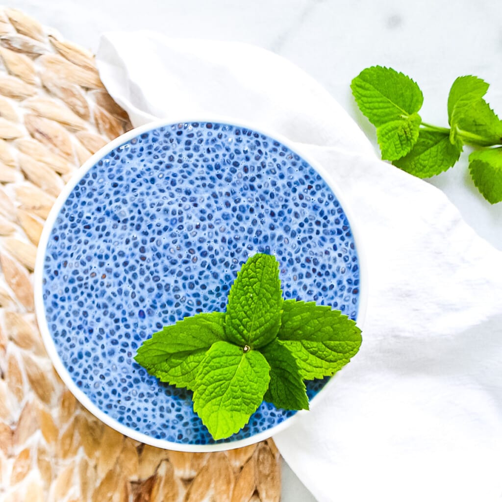 Blue spirulina chia seed pudding in a white bowl, garnished with fresh sprigs of green mint