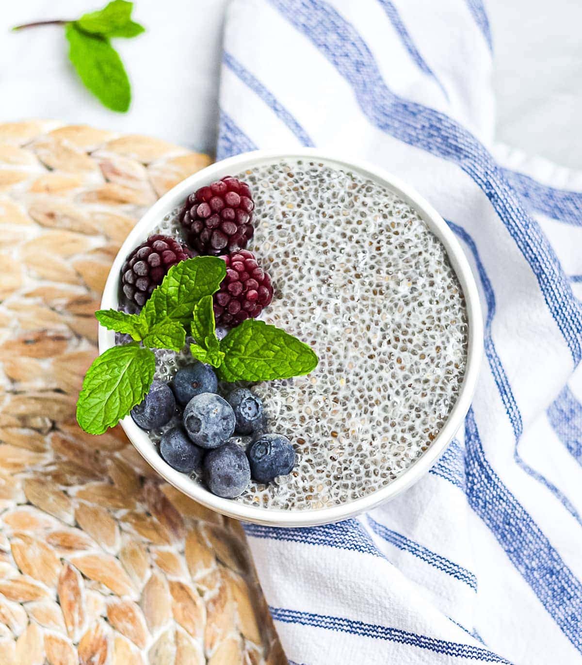 Chia seed pudding in a white bowl garnished with berries and fresh mint sprigs.