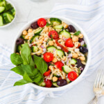 A white bowl sitting on top of a blue and white dish cloth. Inside the bowl is a Mediterranean Orzo Salad with orzo, chickpeas, tomato, olives, sun-dried tomatoes, red onion, and fresh herbs.