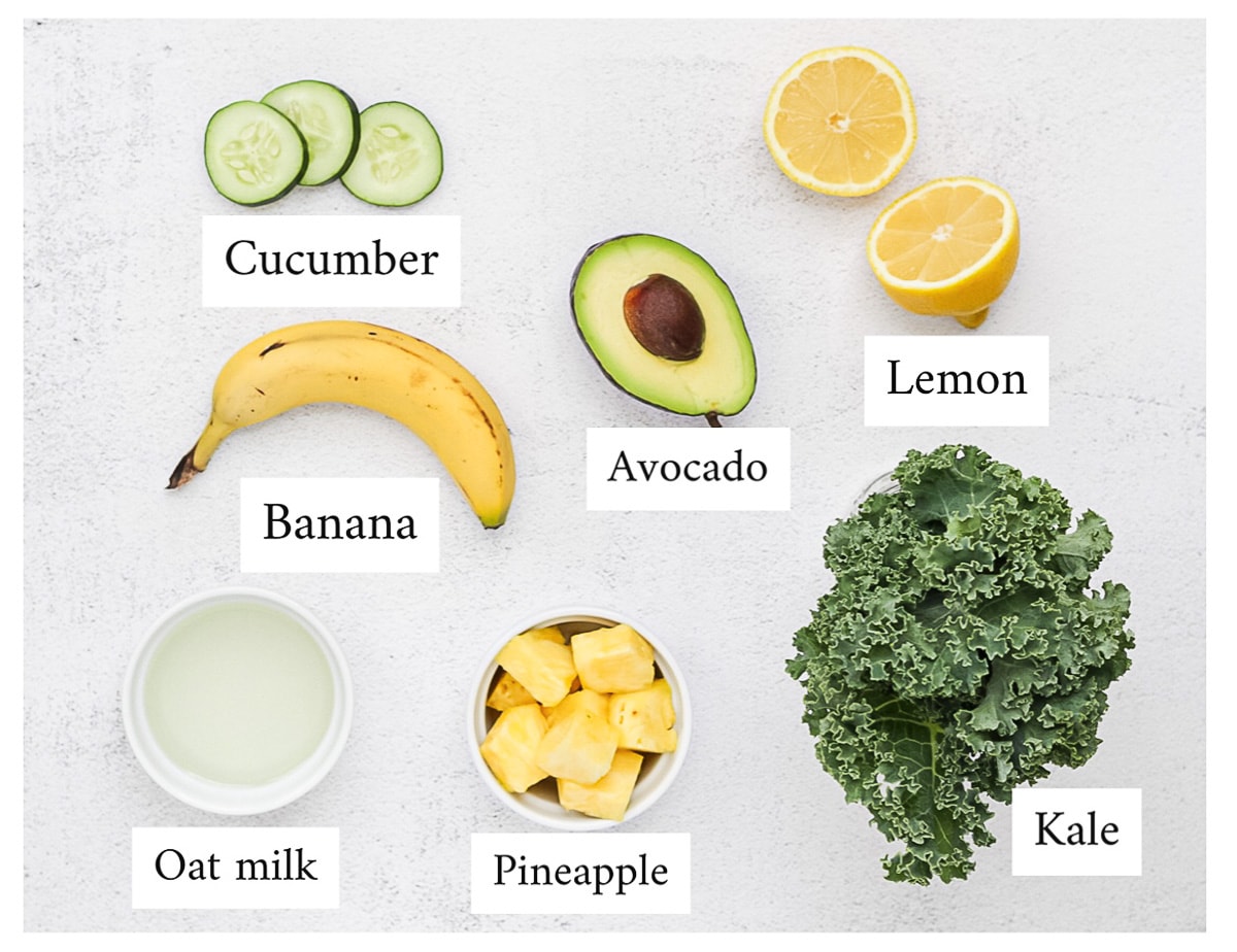 All ingredients are laid out and labeled, including: kale, pineapple, oat milk, lemon, avocado, banana, and cucumber.