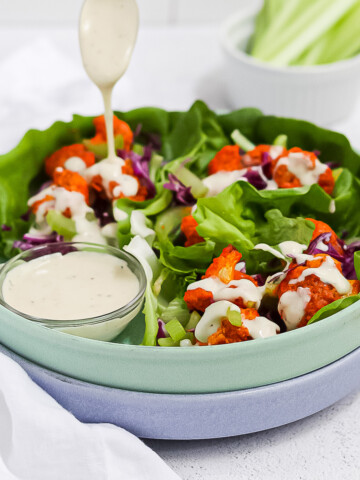 A green bowl filled with cauliflower lettuce wraps with a drizzle of vegan ranch dressing on top.