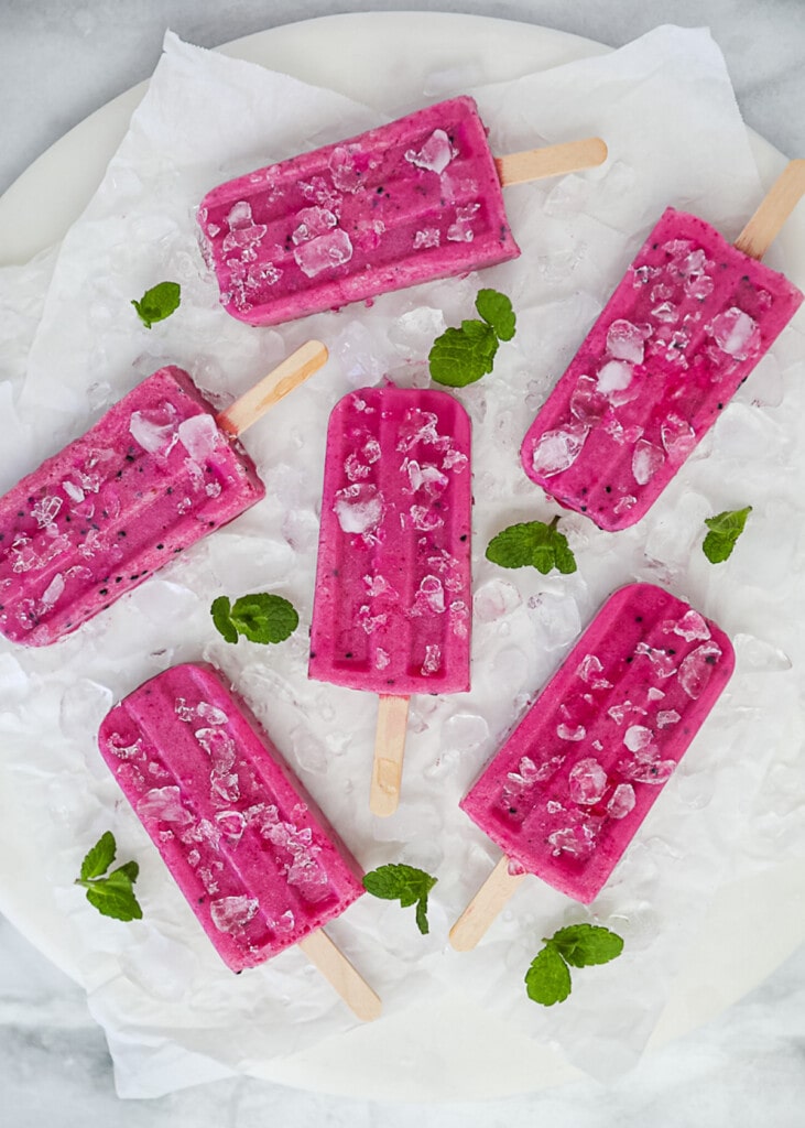 An overhead shot of bright pink popsicles on a white board and white parchment paper.