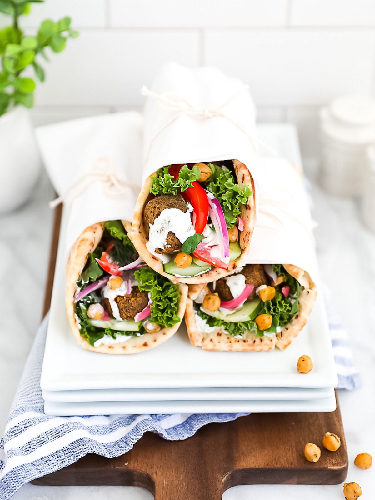 Three pita gyros on a white platter that are filled with falafel, chickpeas, and fresh vegetables.