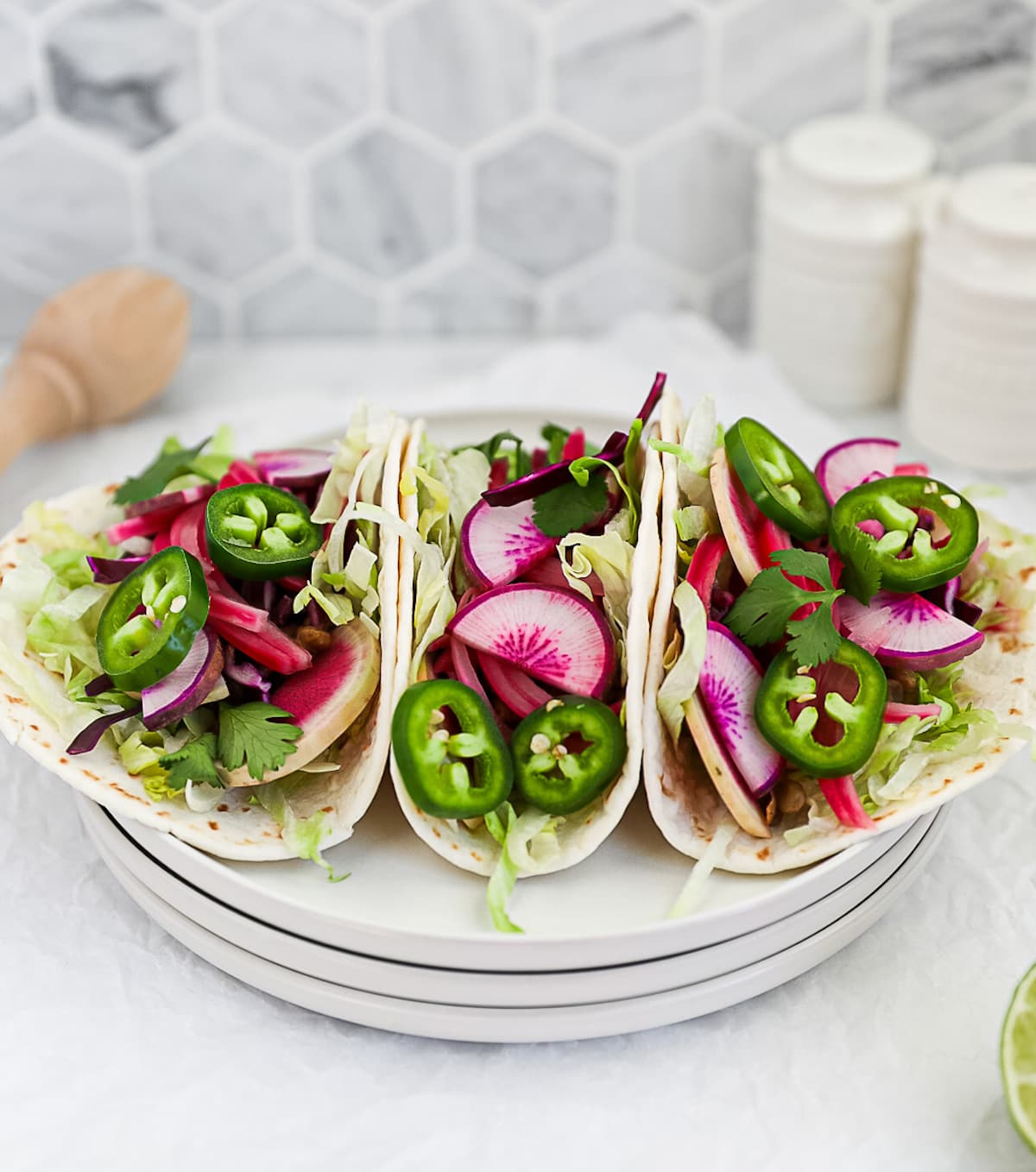 Three tacos filled with vibrant, fresh vegetables including: japalenos, radishes, lettuce, and onions.
