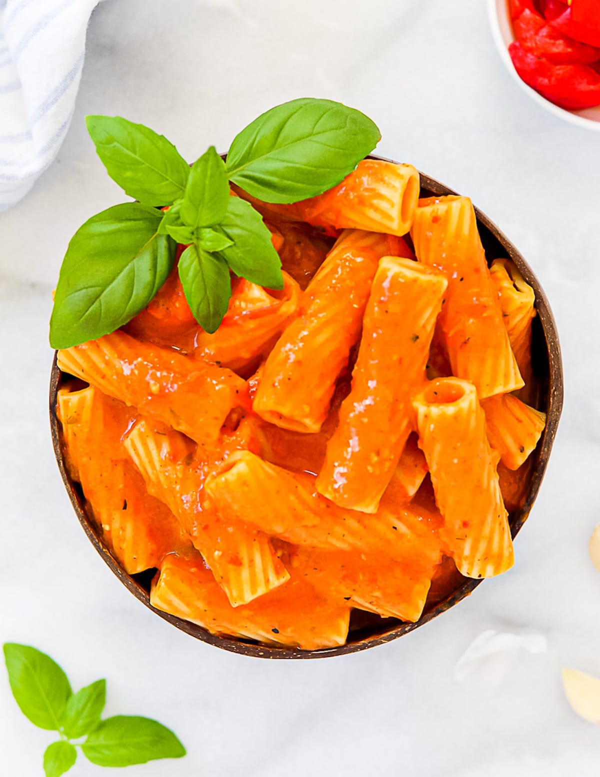 A coconut bowl with rigatoni pasta inside covered with pasta sauce and garnished with fresh basil.