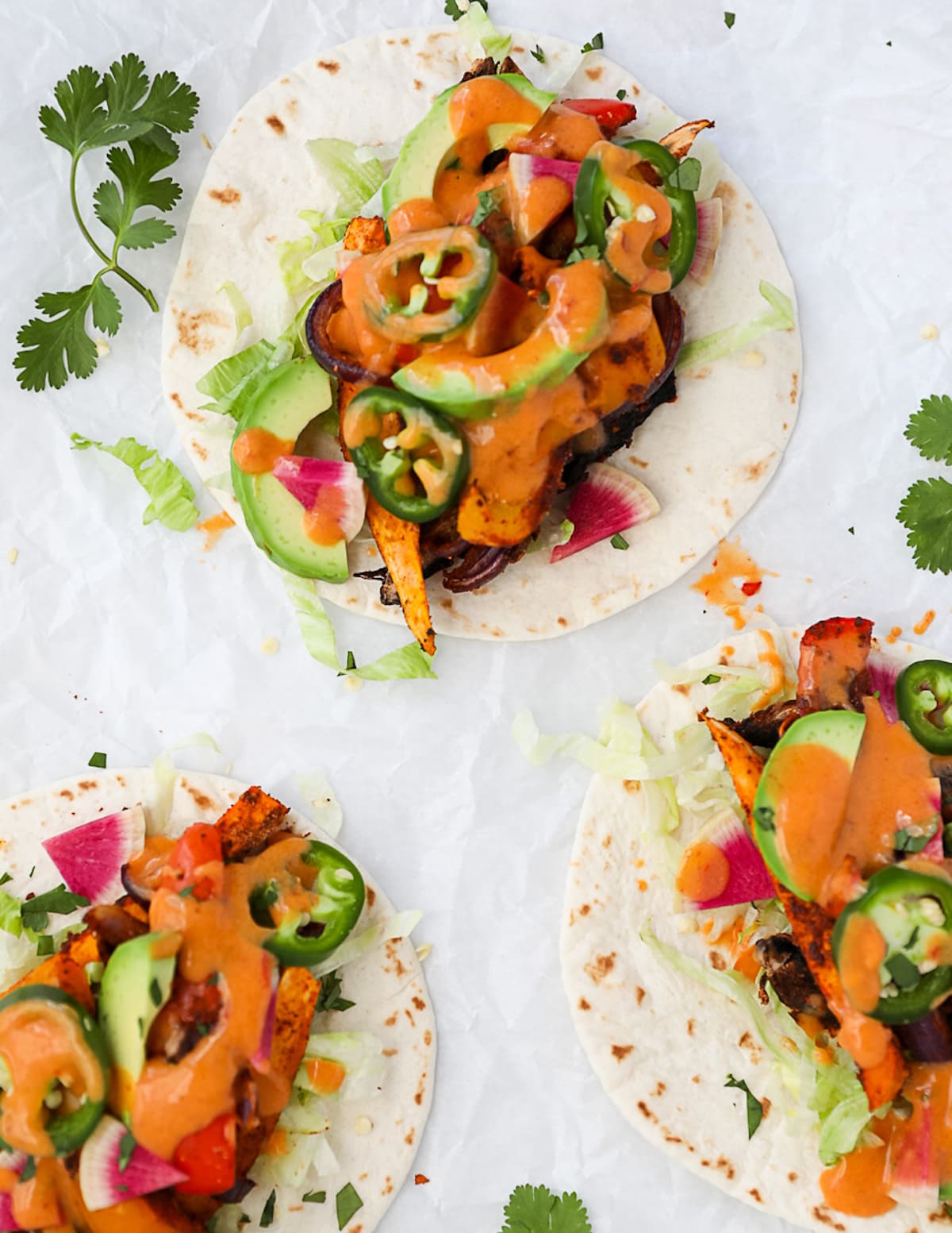Three tacos on white tortillas with roasted and fresh vegetables and a creamy chipotle sauce