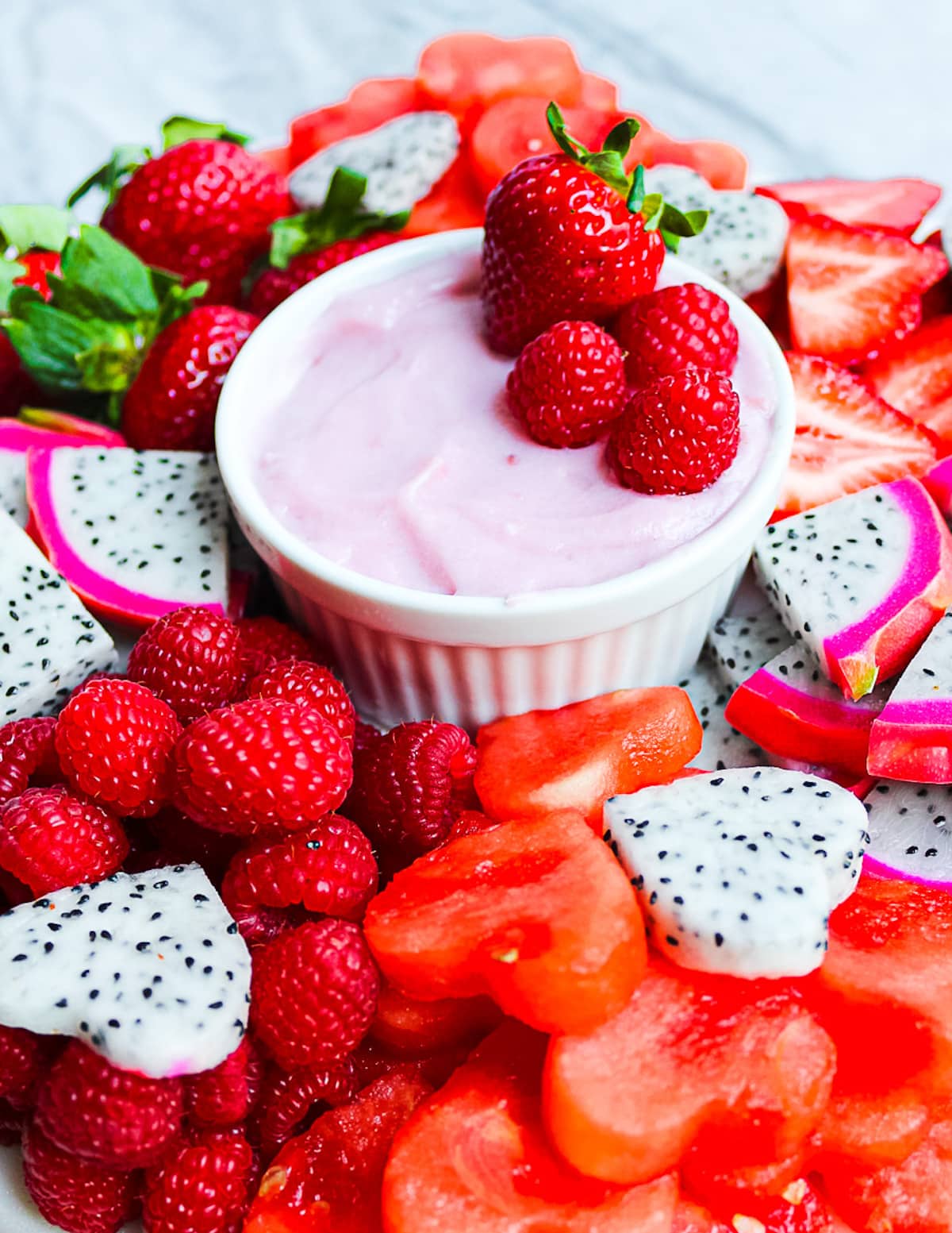 A platter of dragonfruit, strawberries, watermelon, and raspberries with a small white dish filled with a homemade strawberry fruit dip.
