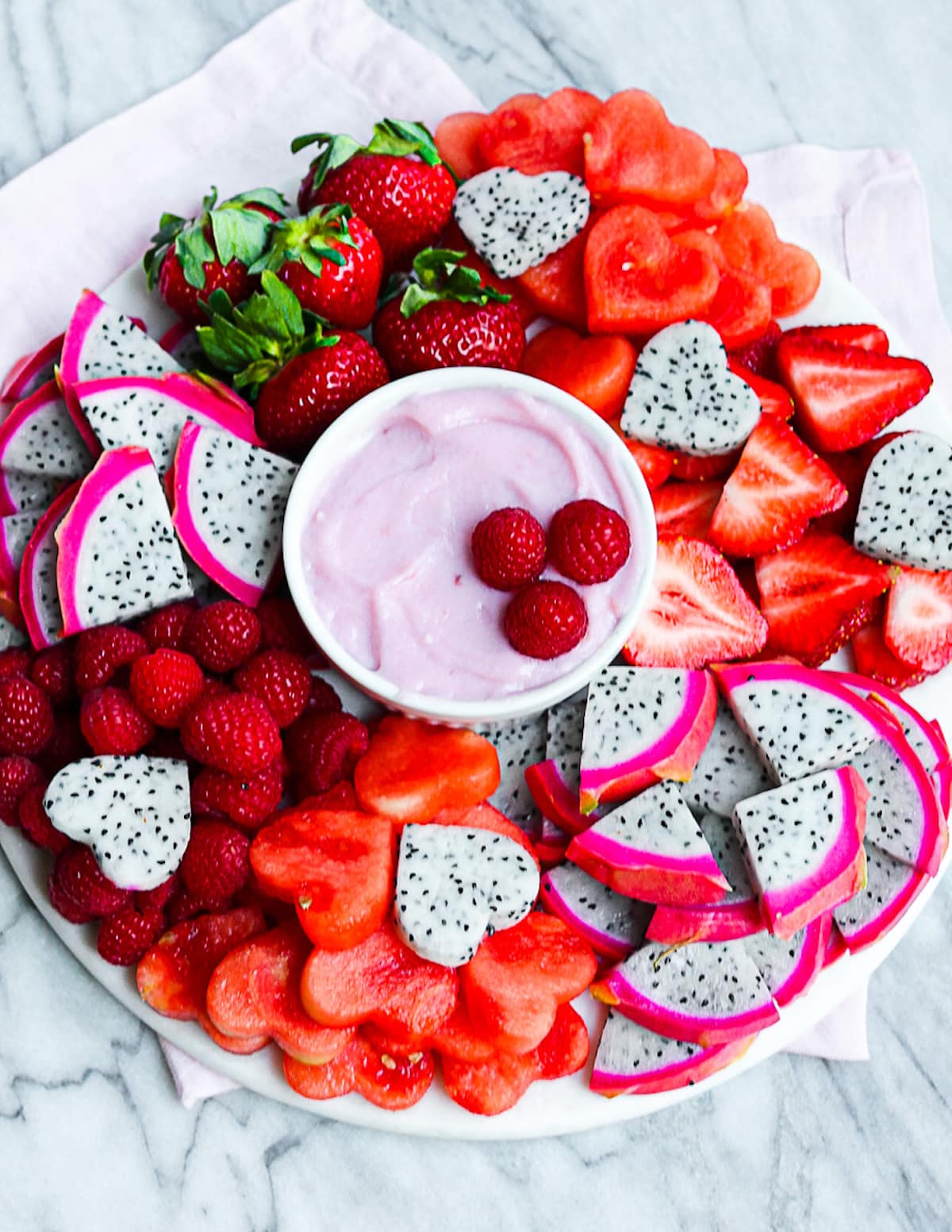 A platter filled with fresh red fruits and with a bowl of dip in the middle
