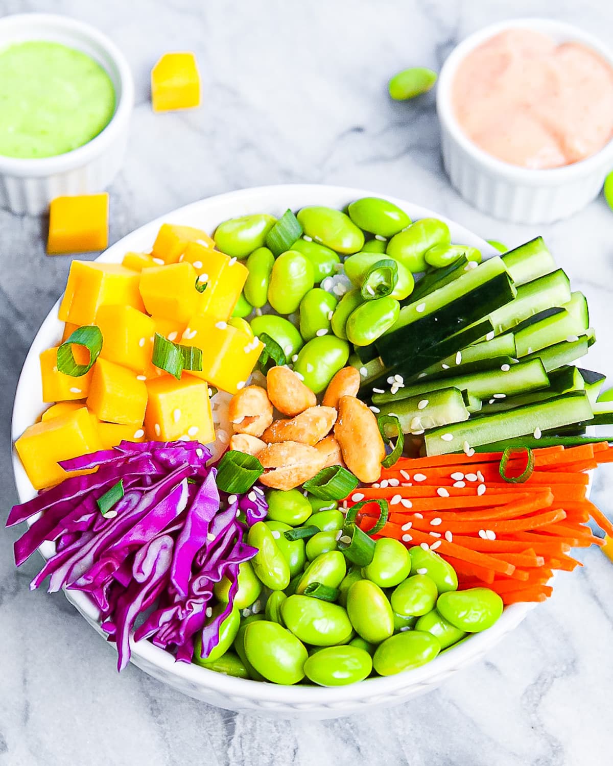 A picture of a sushi bowl with mango, rice, edamame, cucumbers, carrots, cabbage, and peanuts.