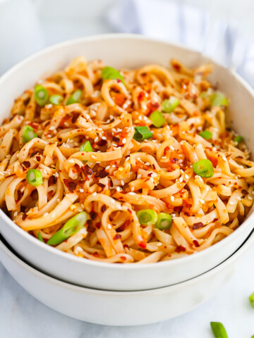 A white bowl filled with spicy chili oil noodles, garnished with sliced green onions.