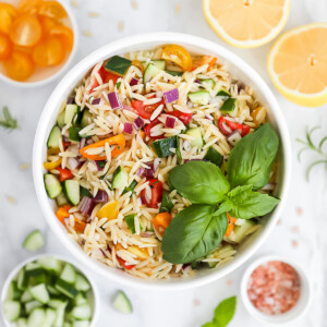 An overhead picture of a bowl of fresh pasta salad filled with fresh vegetables and with a bunch of basil leaves on top.