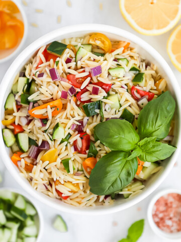 An overhead picture of a bowl of fresh pasta salad filled with fresh vegetables and with a bunch of basil leaves on top.