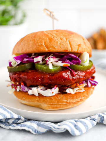 A sandwich with a sauce covered vegan patty, pickles, and coleslaw between two buns.