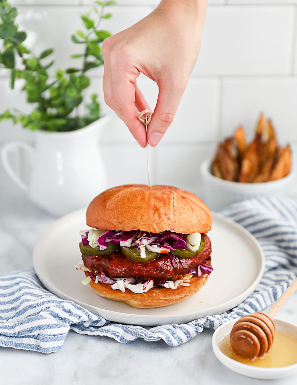 A hand placing a toothpick in a vegan fried chicken sandwich