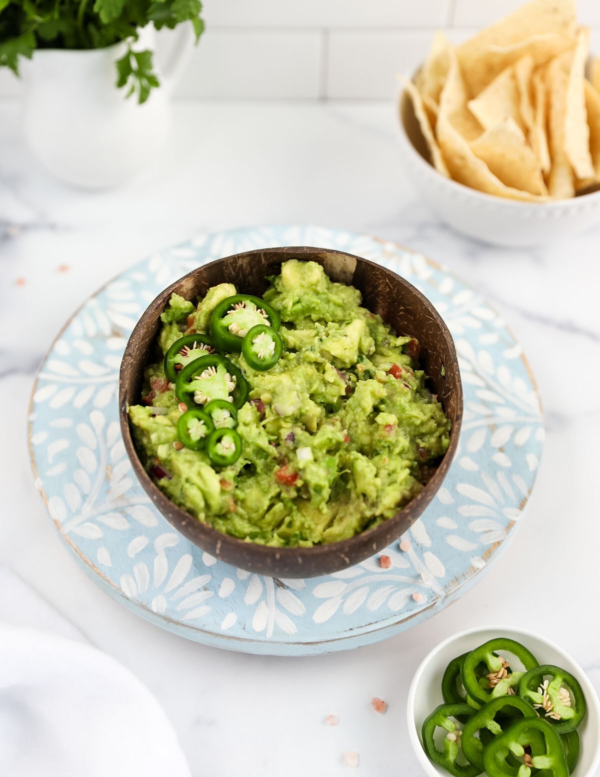 A brown coconut bowl filled with fresh green guacamole, garnished with jalapeno peppers.