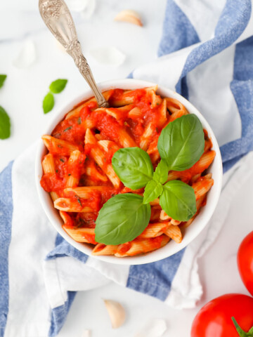 A bowl of pasta and tomato sauce with a fork inside the bowl and basil on top.