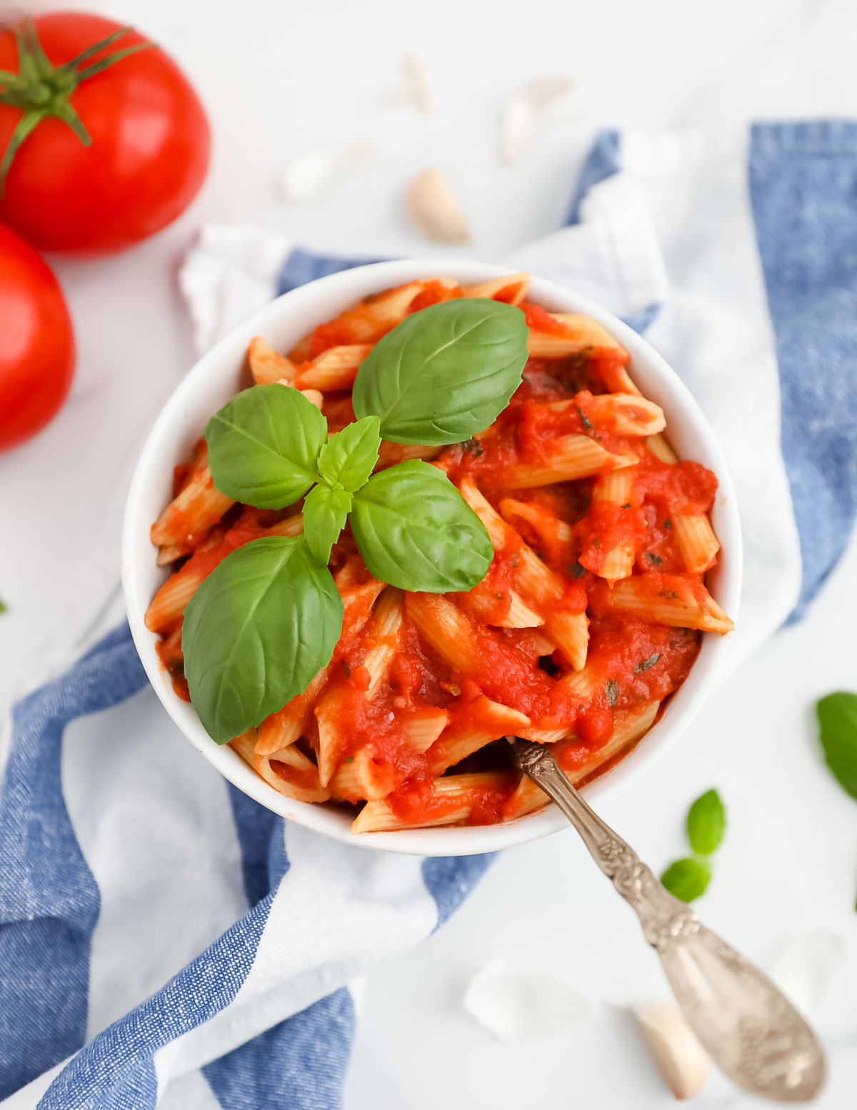 A bowl of penne pasta with pomodoro sauce garnished with a fork and a fresh sprig of green basil