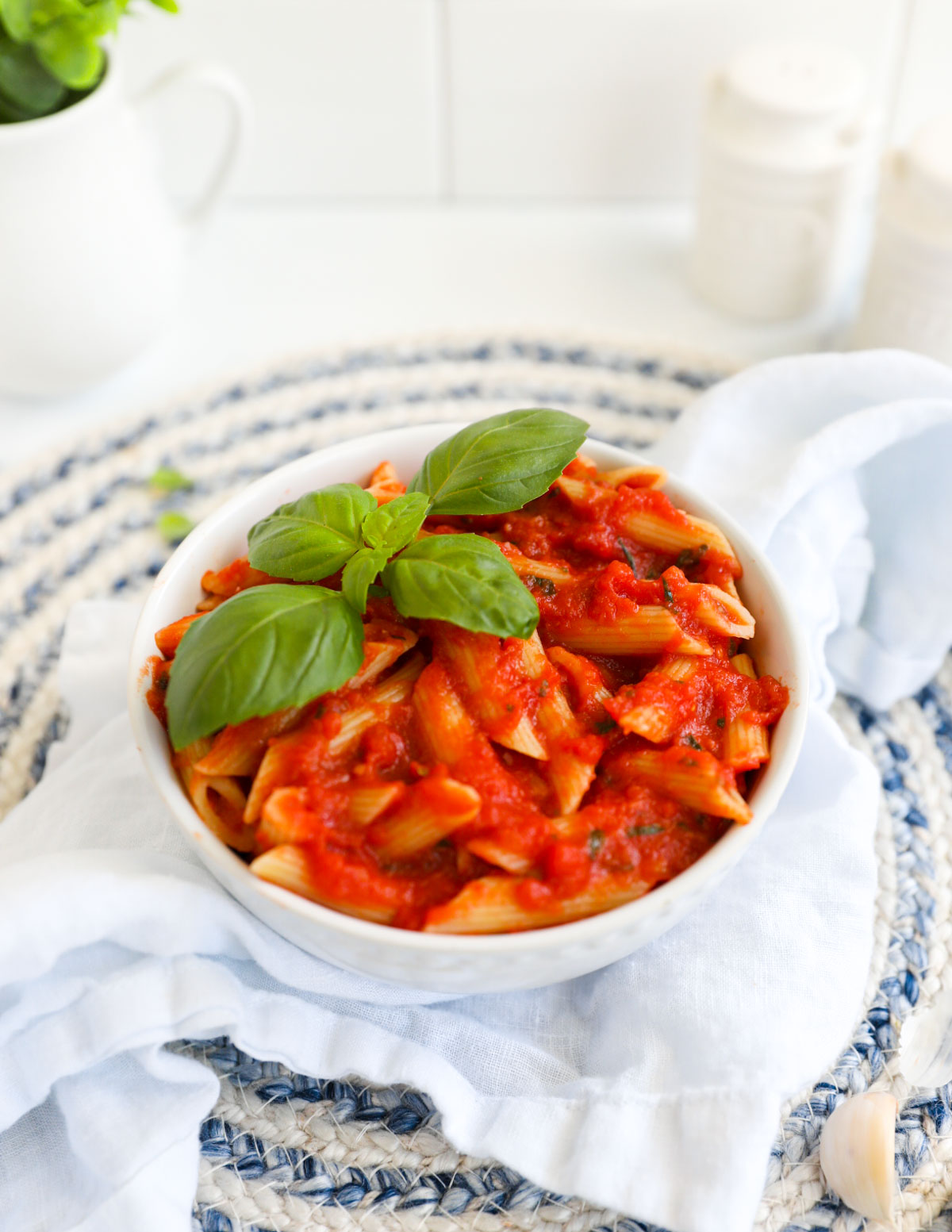 Penne pasta with red pomodoro sauce in a white bowl, garnished with bail.