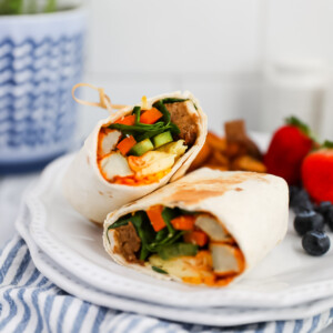 A breakfast burrito that has been sliced in half and is presented on a plate with fresh fruit.