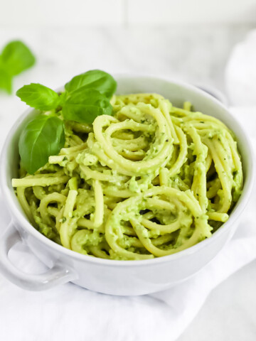 A blue bowl filled with spaghetti noodles covered in a green pesto, garnished with fresh basil