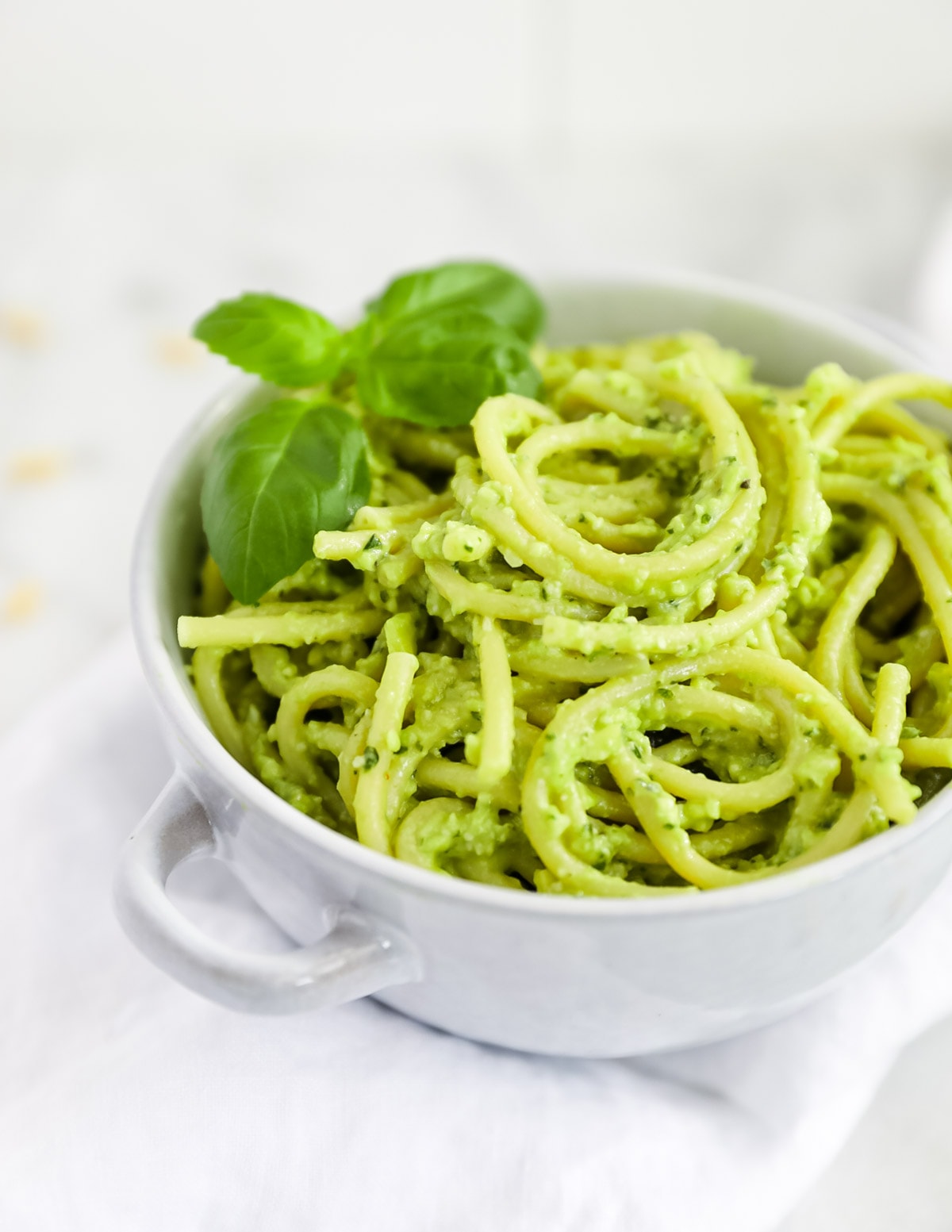 Creamy green pesto over spaghetti noodles, served in a blue bowl and garnished with fresh basil leaves