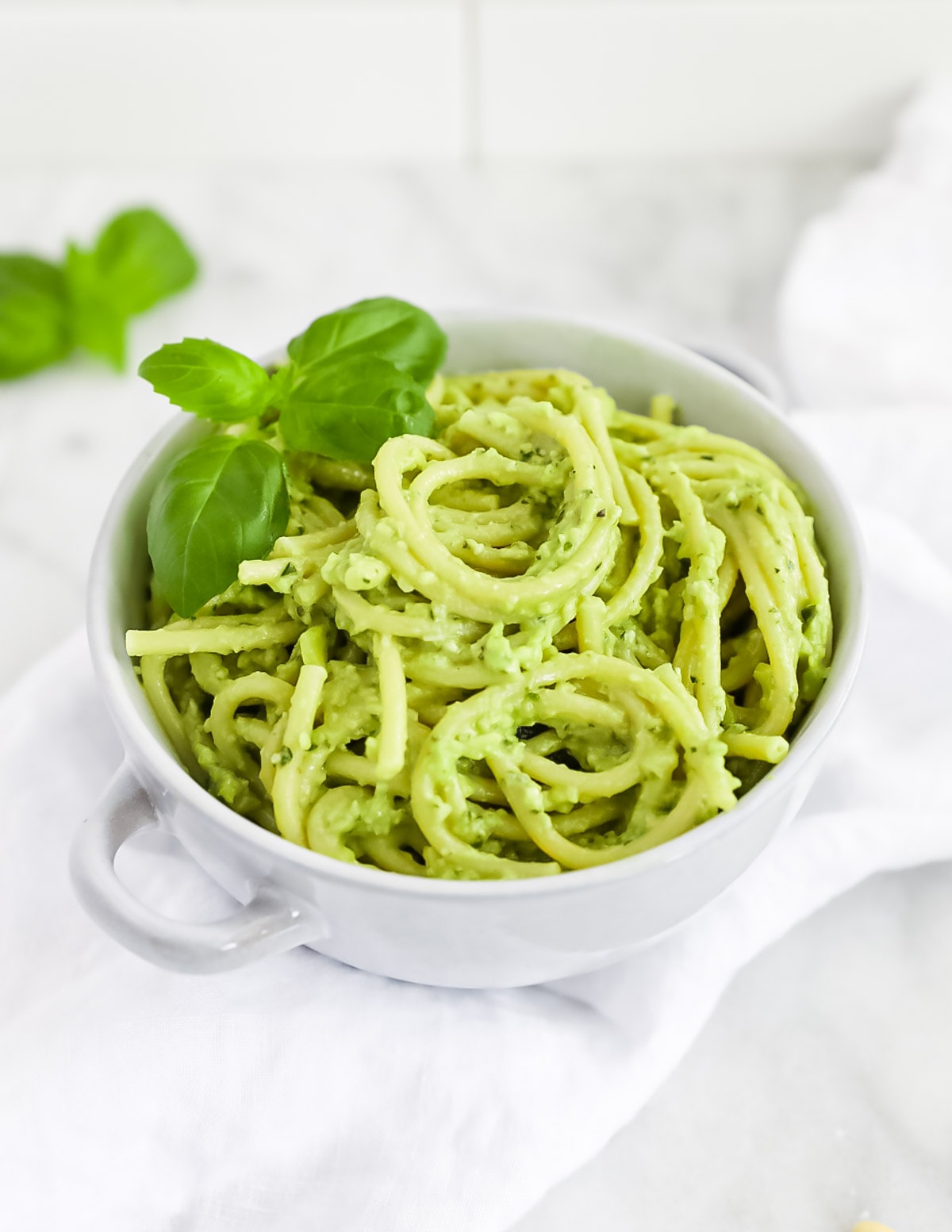 Creamy avocado pesto over thick spaghetti noodles, garnished with fresh basil leaves.