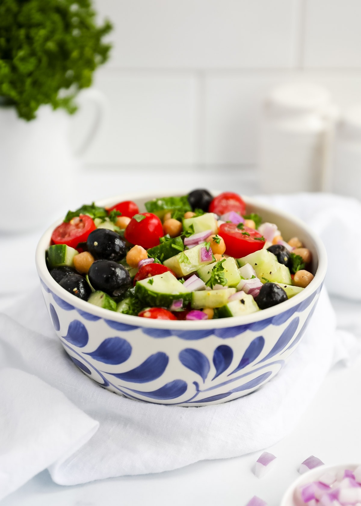 A bowl of cucumber salad with fresh vegetables, chickpeas, olives, and fresh herbs