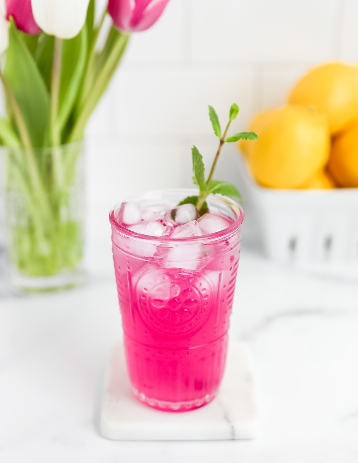 A clear glass filled with bright pink lemonade with ice and a sprig of fresh mint in it
