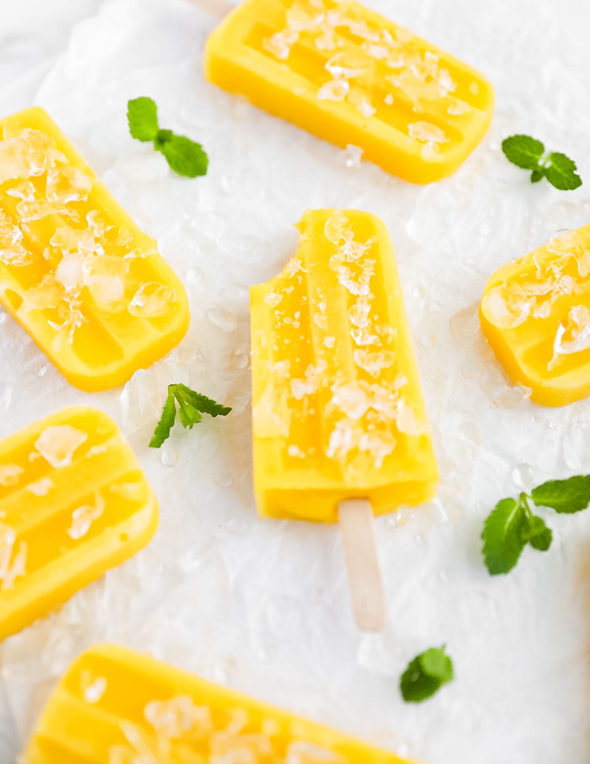 several yellow/orange popsicles, the one in the middle has a bite taken out of it. They are all covered with and surrounded by ice