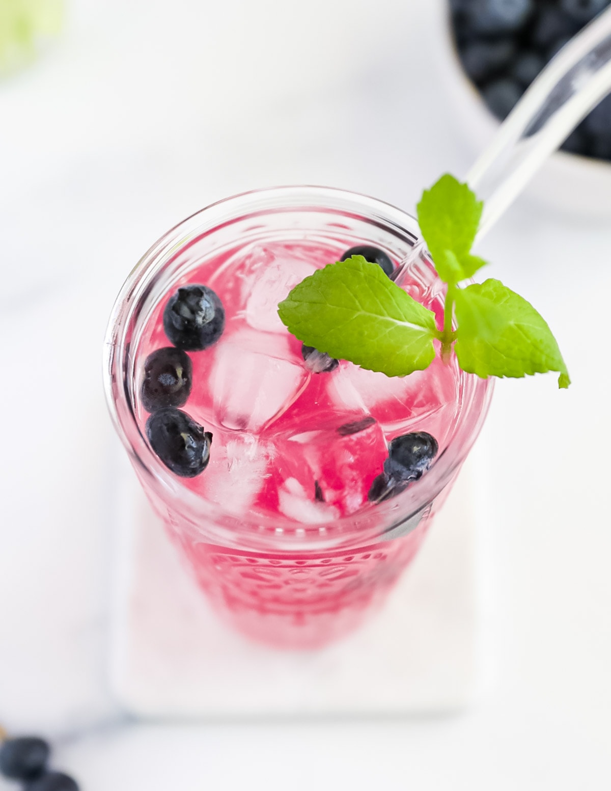 An overhead picture of a glass filled with bright pink lemonade. There are berries, mint, and ice cubes, along with a glass straw in the cup.