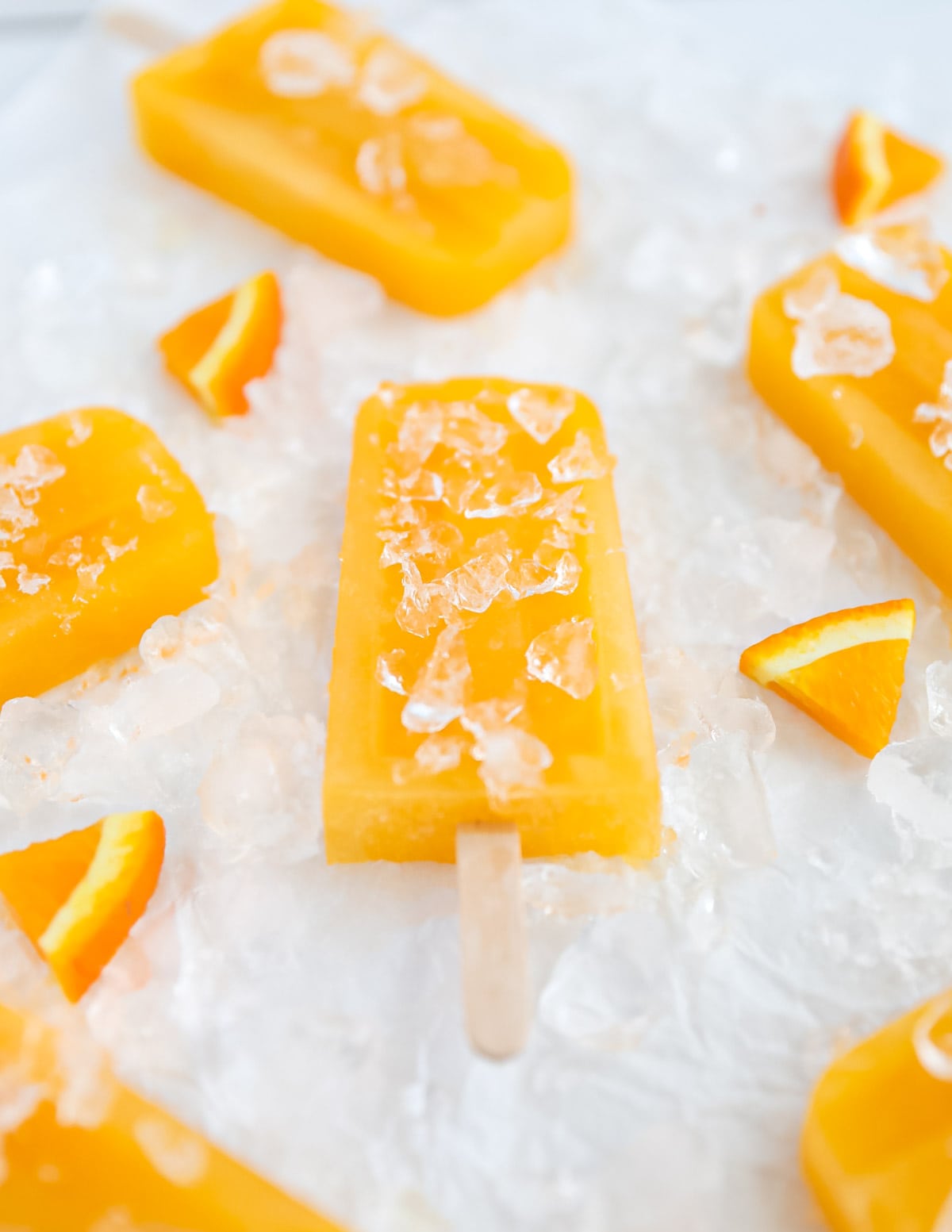 A side angle picture of several orange ice pops, resting on a bed of crushed ice.