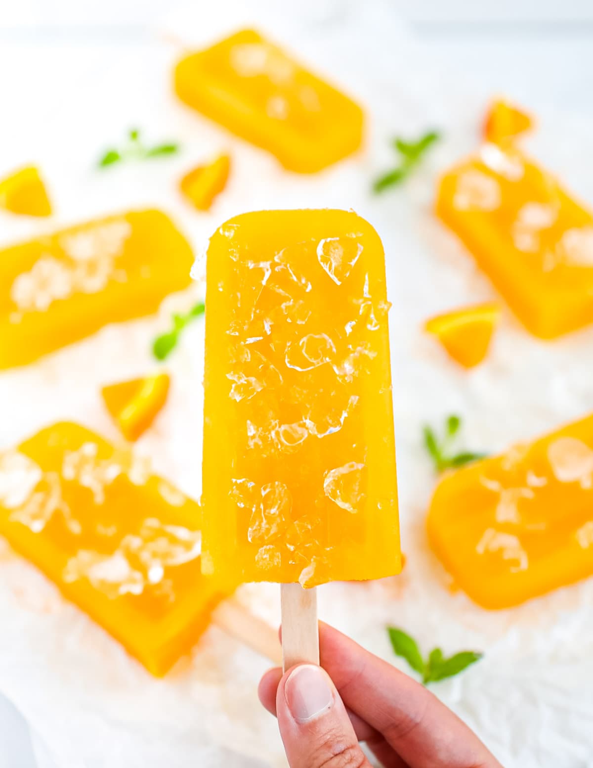 A hand holding up an orange-yellow ice pop that is covered in ice