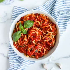 An overhead picture of a white bowl filled with spaghetti and red sauce, it is garnished with a sprig of fresh green basil.