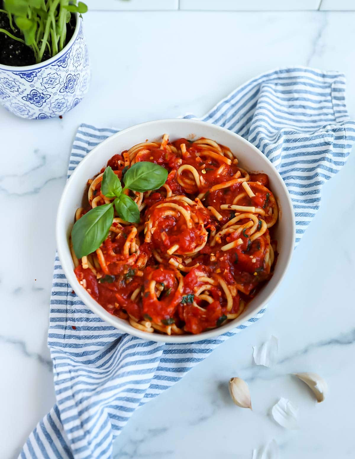 Red sauce covering spaghetti in a white bowl. The spaghetti is garnished with fresh green basil