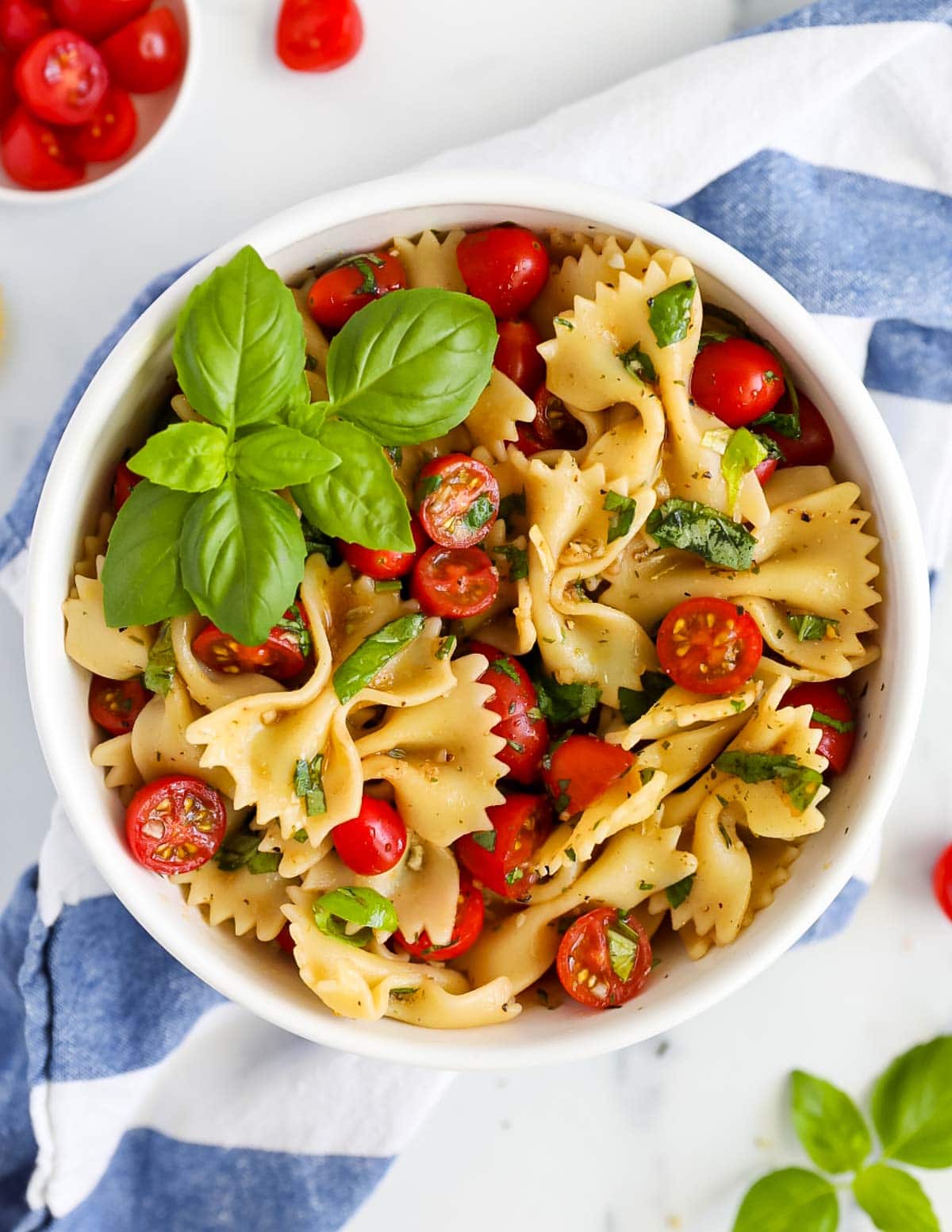 A bowl filled with bowtie pasta, cherry tomatoes, and fresh basil