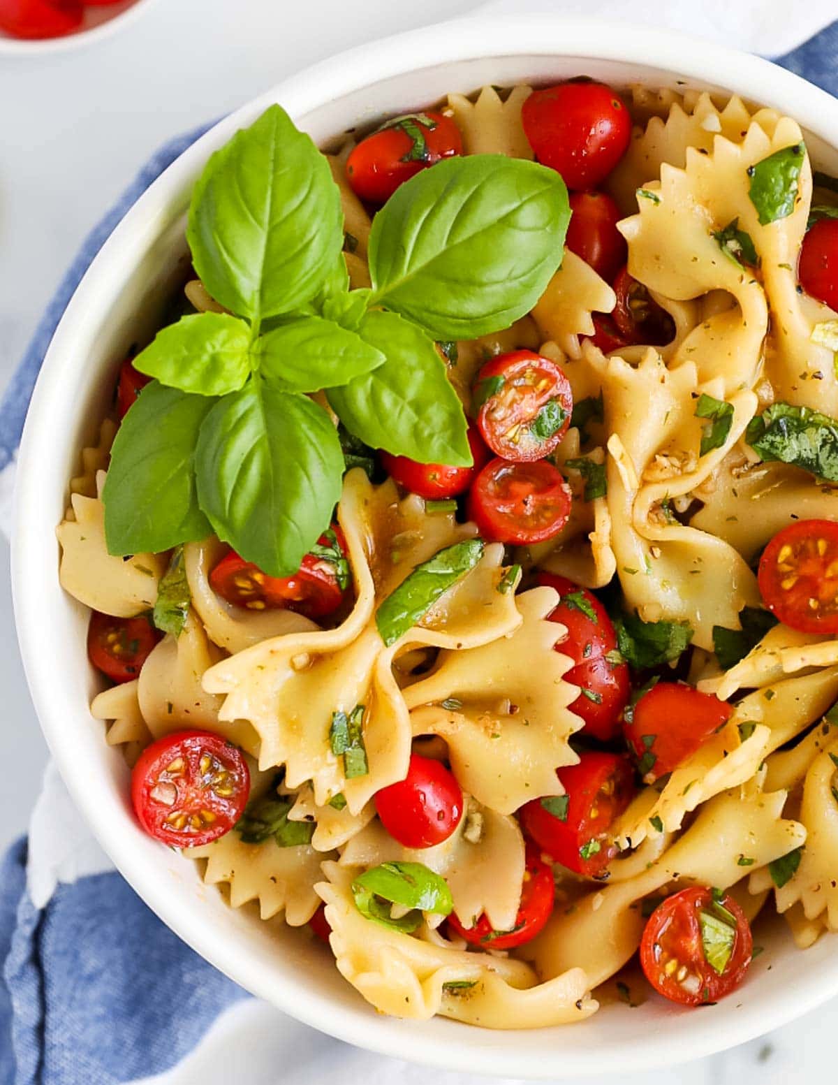 A close-up picture of a white bowl filled with pasta, tomatoes, and fresh green basil