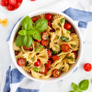 A bowl filled with bowtie pasta, sliced cherry tomatoes, and fresh basil