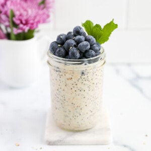 A mason jar filled with overnight oatmeal and topped with blueberries and fresh mint