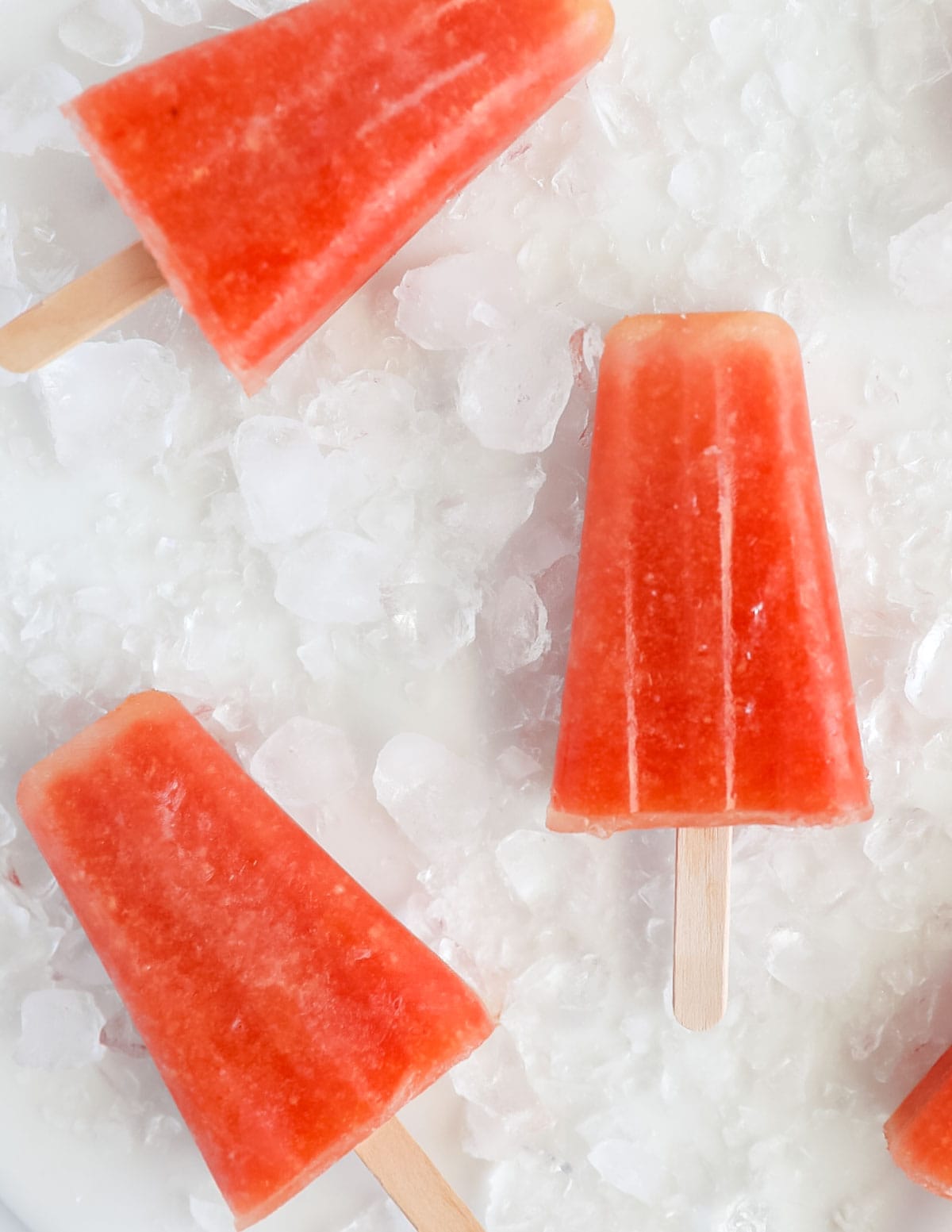 Three pink popsicles on a bed of crushed ice