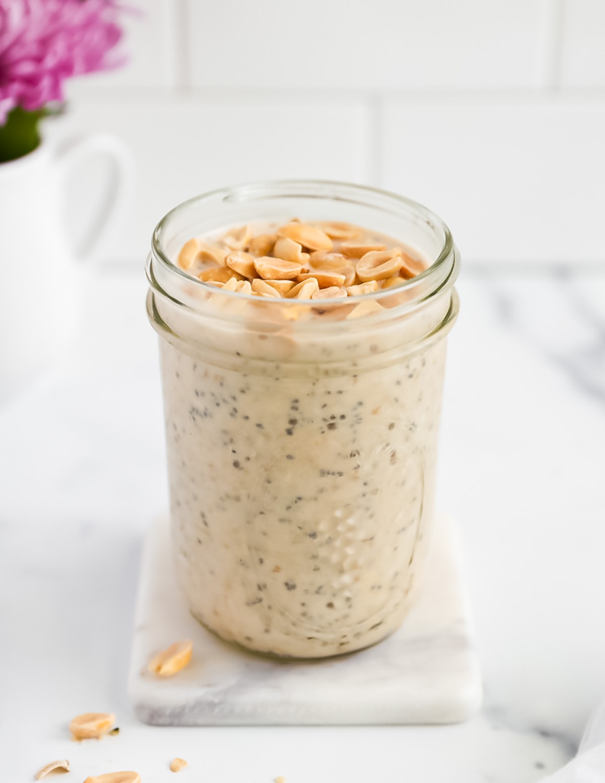 A close up picture of a glass jar filled with peanut butter overnight oats with chia seeds, there are peanuts on top.