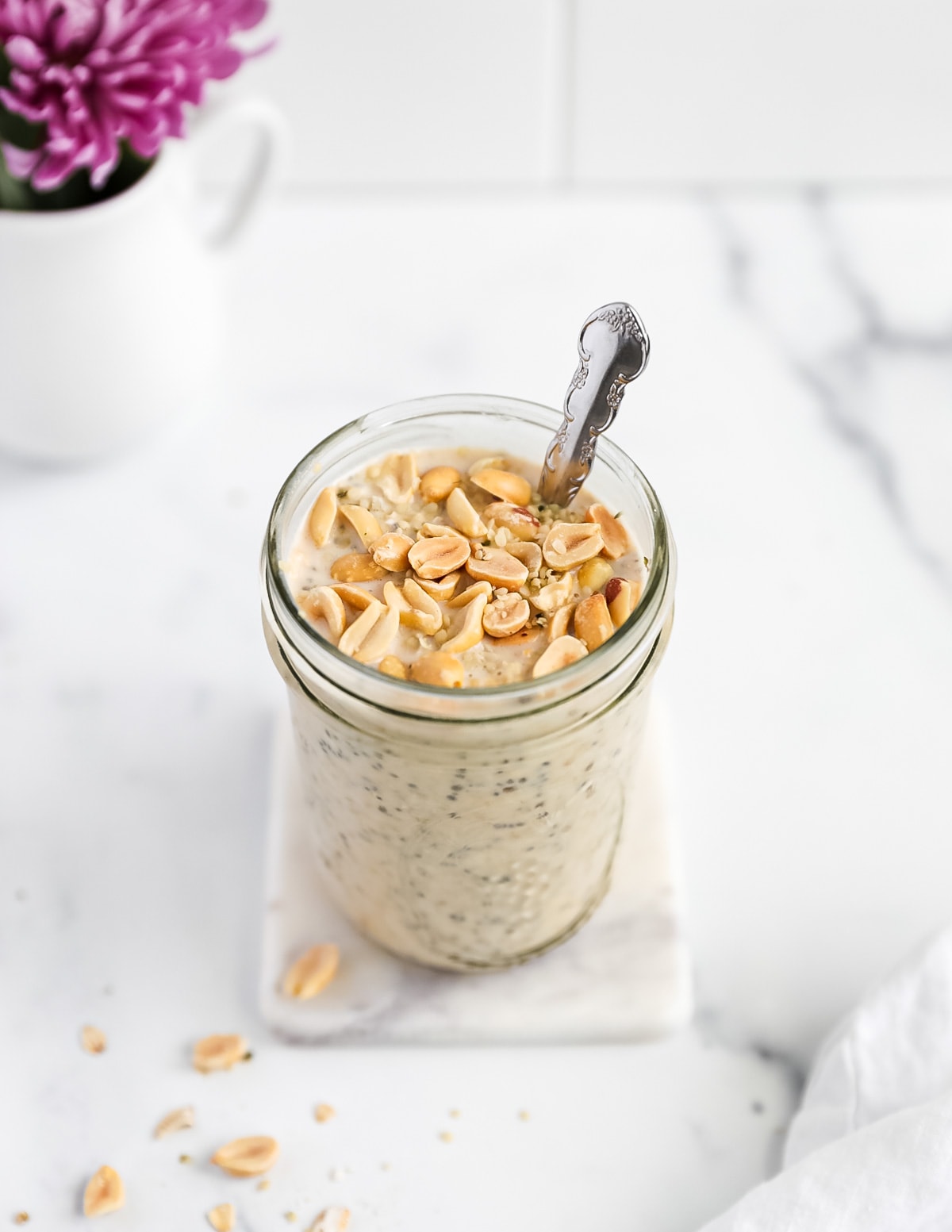 An overhead shot of a jar filled with overnight oats, the oats are topped with peanuts and hemp seeds, there is a spoon in the jar