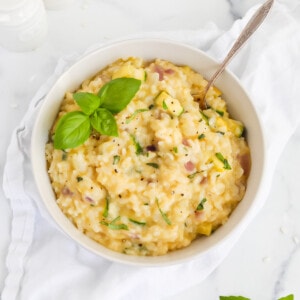 A bowl of risotto with vegetables inside and garnished with fresh basil