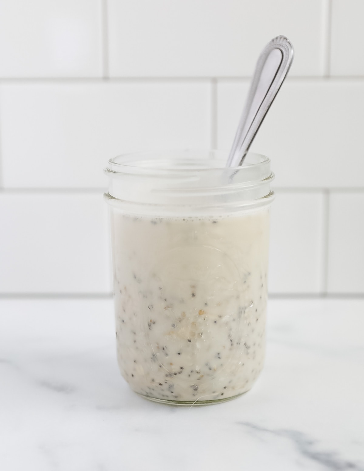 A mason jar with unmixed oatmeal and plant based milk. There is a spoon in the jar