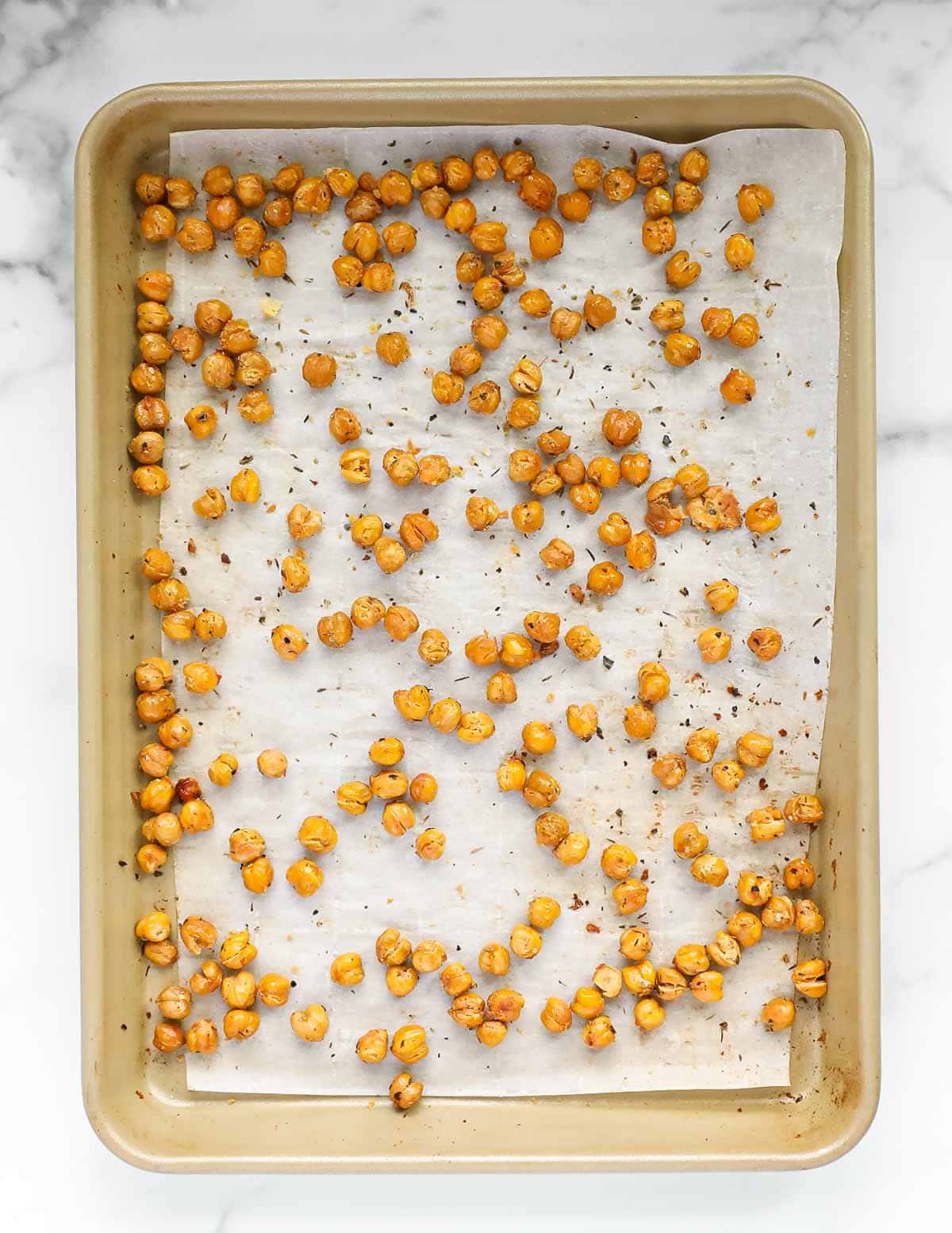 Chickpeas spread out on a piece of white parchment paper on a gold backing sheet.