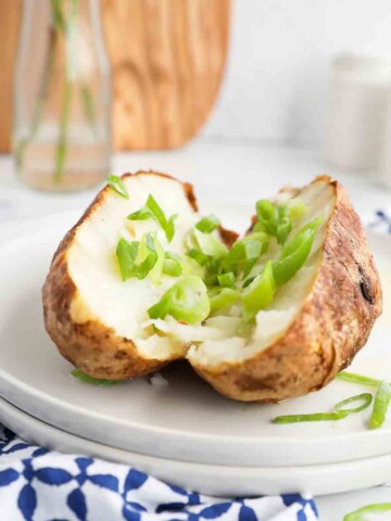 A baked potato that is sliced open and covered in sliced green onions