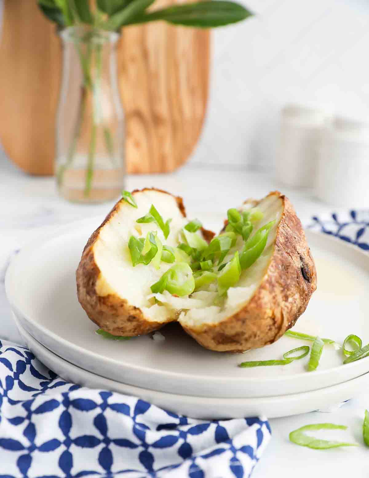 A sliced baked potato covered in sliced green onions on two stacked white plates.