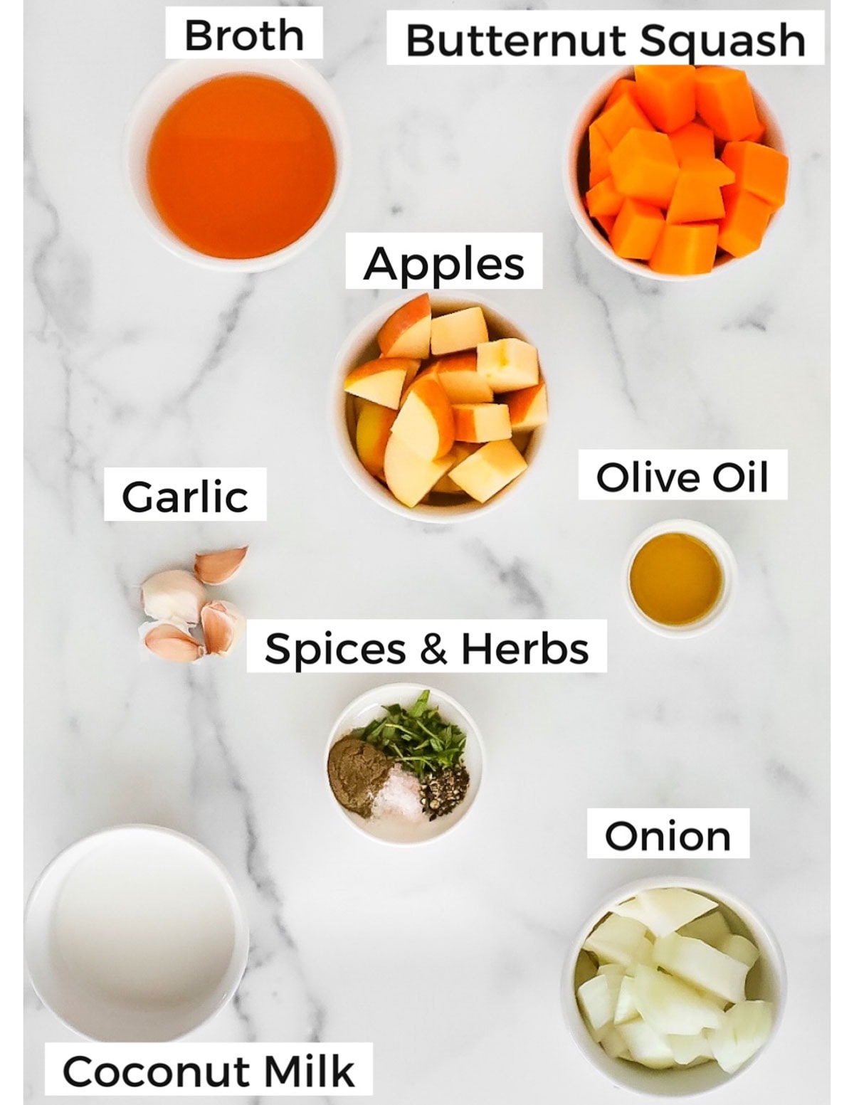 Labeled ingredients in small white bowls including: broth, butternut squash, apples, olive oil, garlic, spices and herbs, onion, and coconut milk
